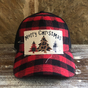 Red and black plaid cap with a 'Merry Christmas' patch featuring trees on a wooden surface.
