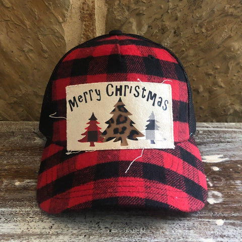Red and black plaid cap with a 'Merry Christmas' patch featuring trees on a wooden surface.