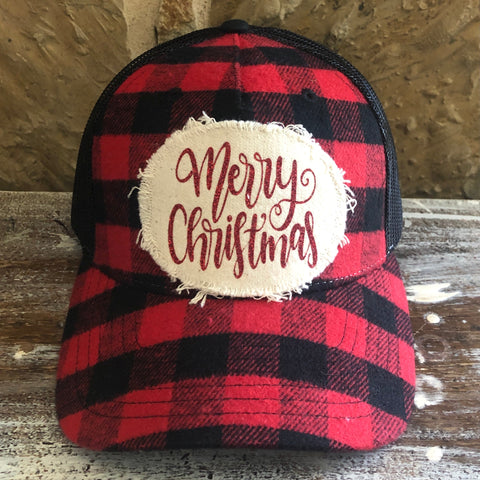Red and black plaid cap with 'Merry Christmas' patch on a wooden surface.