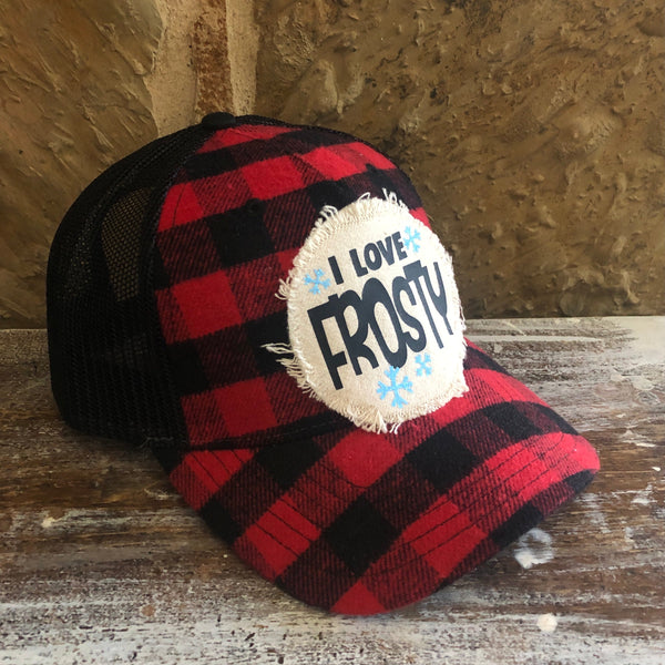 Red and black plaid cap with 'I Love Frosty' patch on a wooden surface.