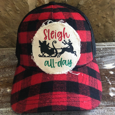 Red and black plaid cap with 'Sleigh all day' patch on a rustic surface
