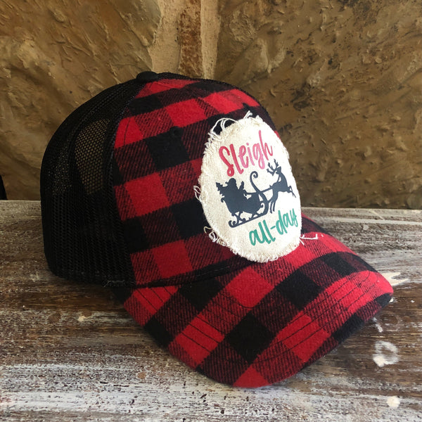 Red and black plaid cap with 'Sleigh all day' text on a wooden surface.