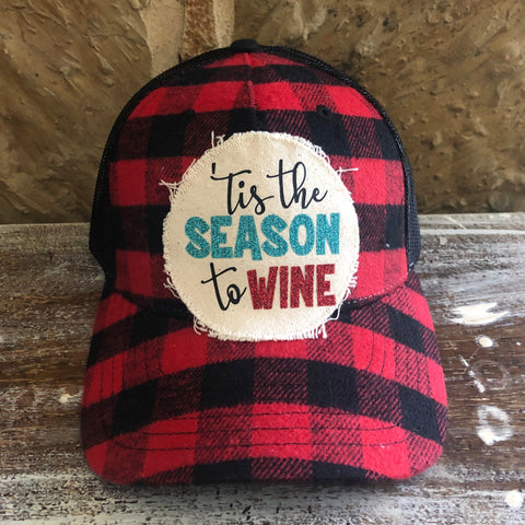 Red and black checkered cap with 'Tis the Season to Wine' text on a wooden surface.