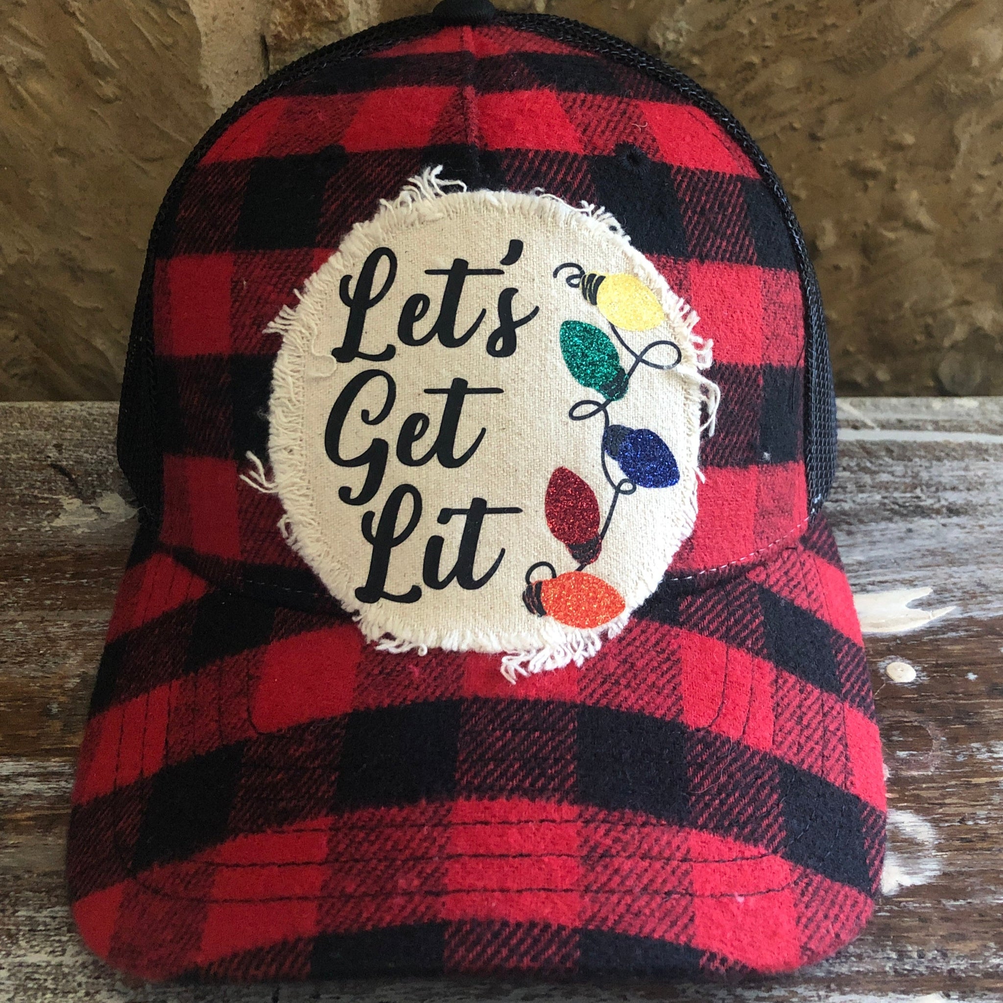 Red and black plaid cap with 'Let's Get Lit' patch on a wooden surface