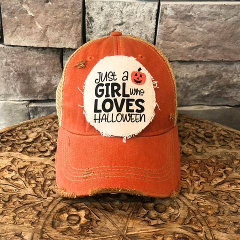 Orange cap with a patch that reads 'Just a Girl Who Loves Halloween' on a wooden surface.