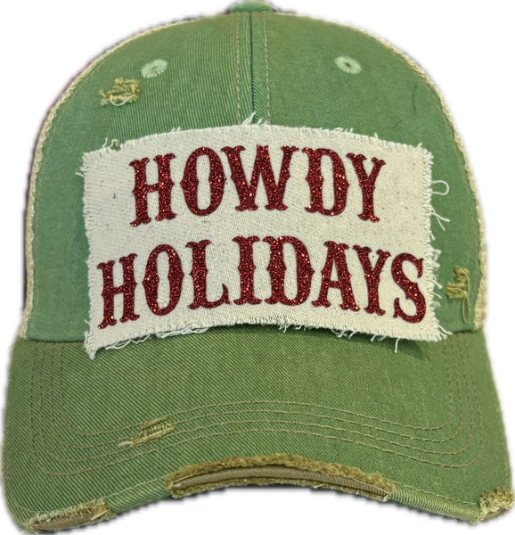 A green vintage-style 'Howdy Holidays' trucker hat with red glitter text on the front.