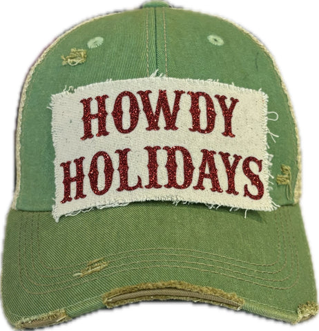 A green vintage-style 'Howdy Holidays' trucker hat with red glitter text on the front.