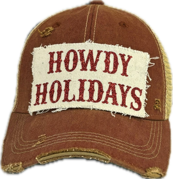 A brick red vintage-style 'Howdy Holidays' trucker hat with red glitter text on the front.