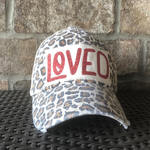 A vintage-style baseball cap with 'LOVED' text in red across the front, featuring a leopard print pattern 