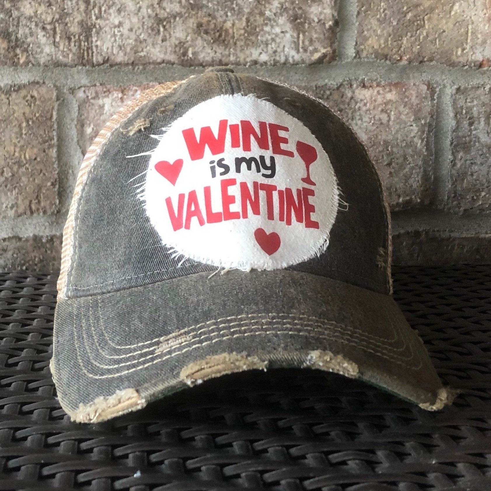 A distressed black baseball cap with an oversized red 'WINE IS MY VALENTINE' text logo.
