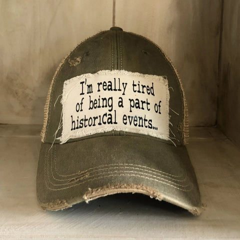 A green baseball cap with a white text label that reads 'I'm Really Tired of being part of Historical Events.'